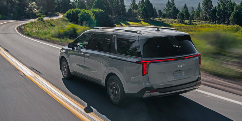 Rear view of Kia Carnival driving on a curvy road.