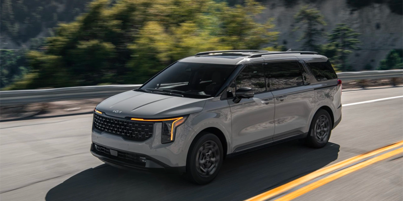 Front-side view of Kia Carnival driving on a highway.
