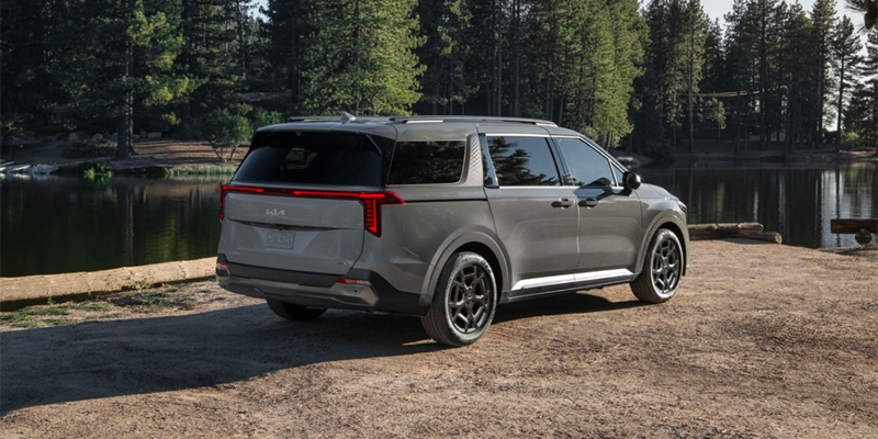 A gray SUV is parked next to a lake, with trees in the background