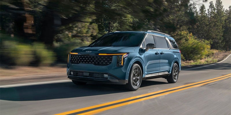 A blue SUV drives down a winding road, with trees on both sides