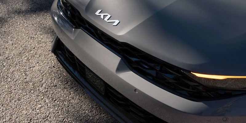 Close-up of the Kia K5 front grille and hood with the Kia logo and LED headlight detail.