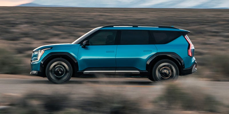 A blue Kia EV9 in motion on a desert road