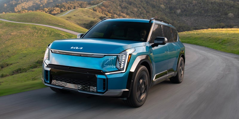 A blue Kia EV9 driving on a winding, hilly road