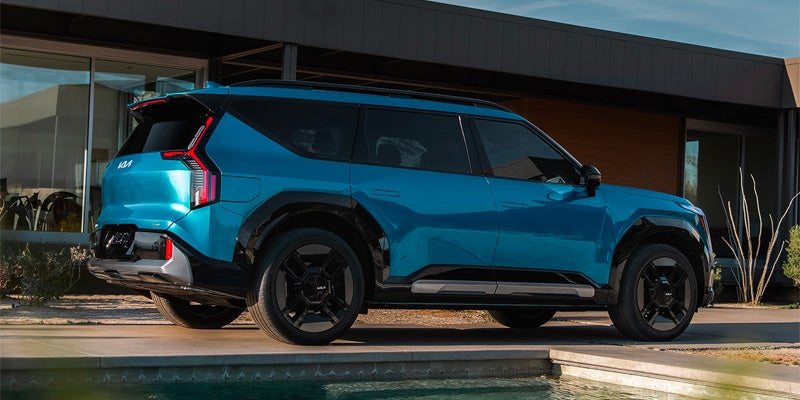 A blue Kia EV9 parked next to a modern house and pool