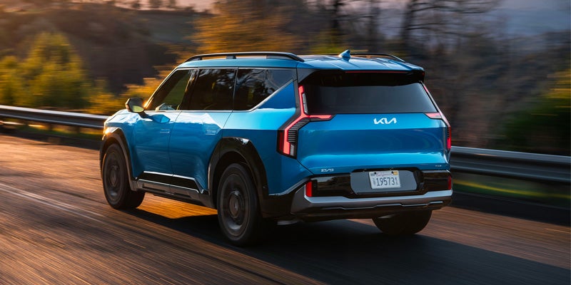 The back of a blue Kia EV9 driving on a winding road