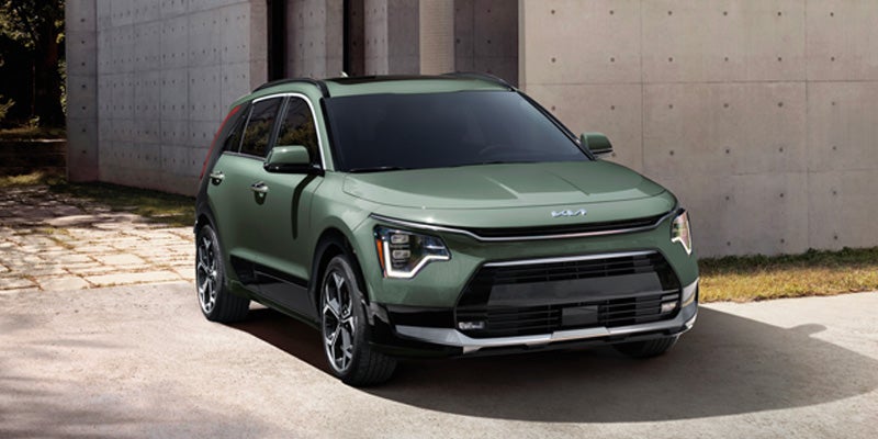 A green Kia Niro EV parked in front of a modern building