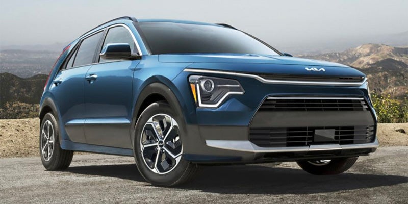 A blue Kia Niro EV parked in a mountainous, rural landscape.