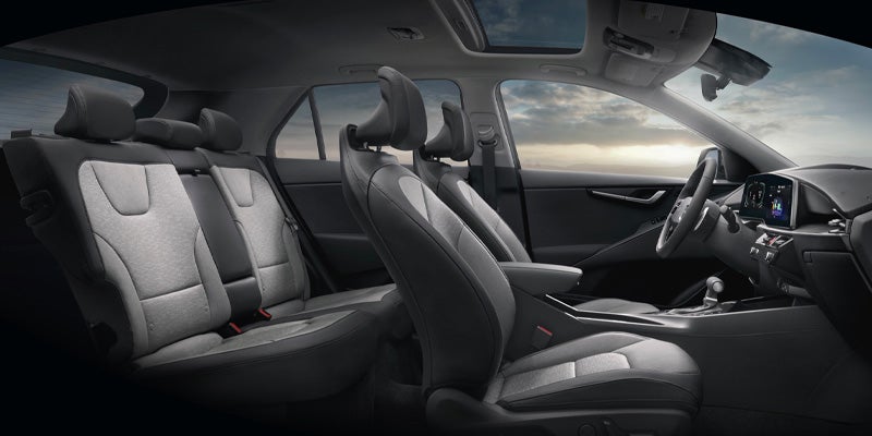 The car's interior, specifically the front and back seats, with a view of the sky through the sunroof
