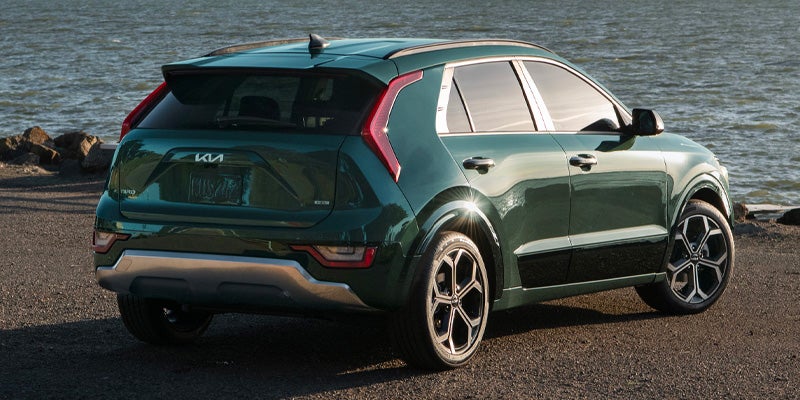 The rear of a green Kia Niro EV parked by a body of water