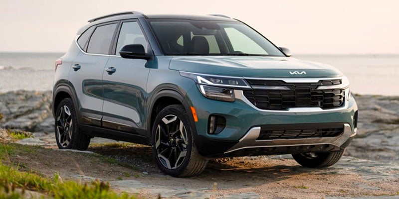A green Kia Seltos parked on a rocky beach