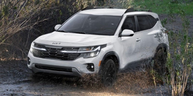 A white Kia Seltos driving through mud