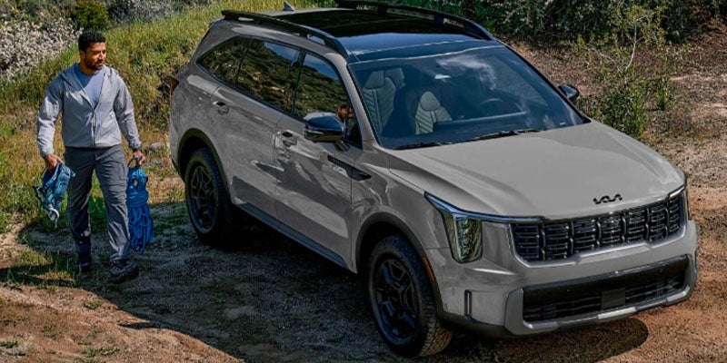 A man stands beside a gray SUV in a rustic setting