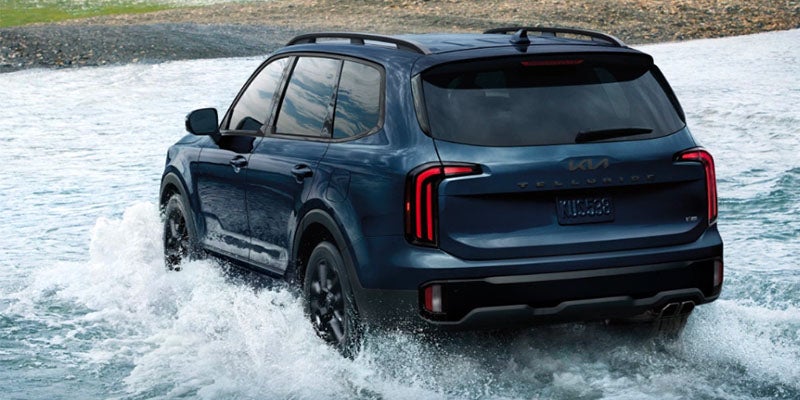 A blue Kia Telluride driving through a shallow stream