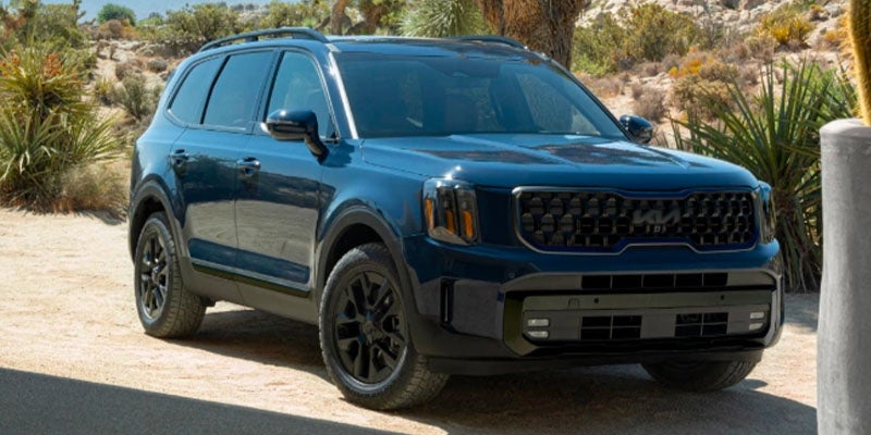 The front of a blue Kia Telluride on a dirt road
