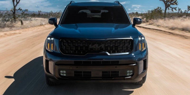 The front of a dark blue Kia Telluride on a dirt road
